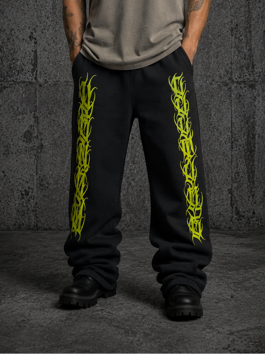 black sweatpants featuring bright green and yelllow calligraphy style graphics spelling venom and culture down the sides, standing against a dark textured concrete wall.