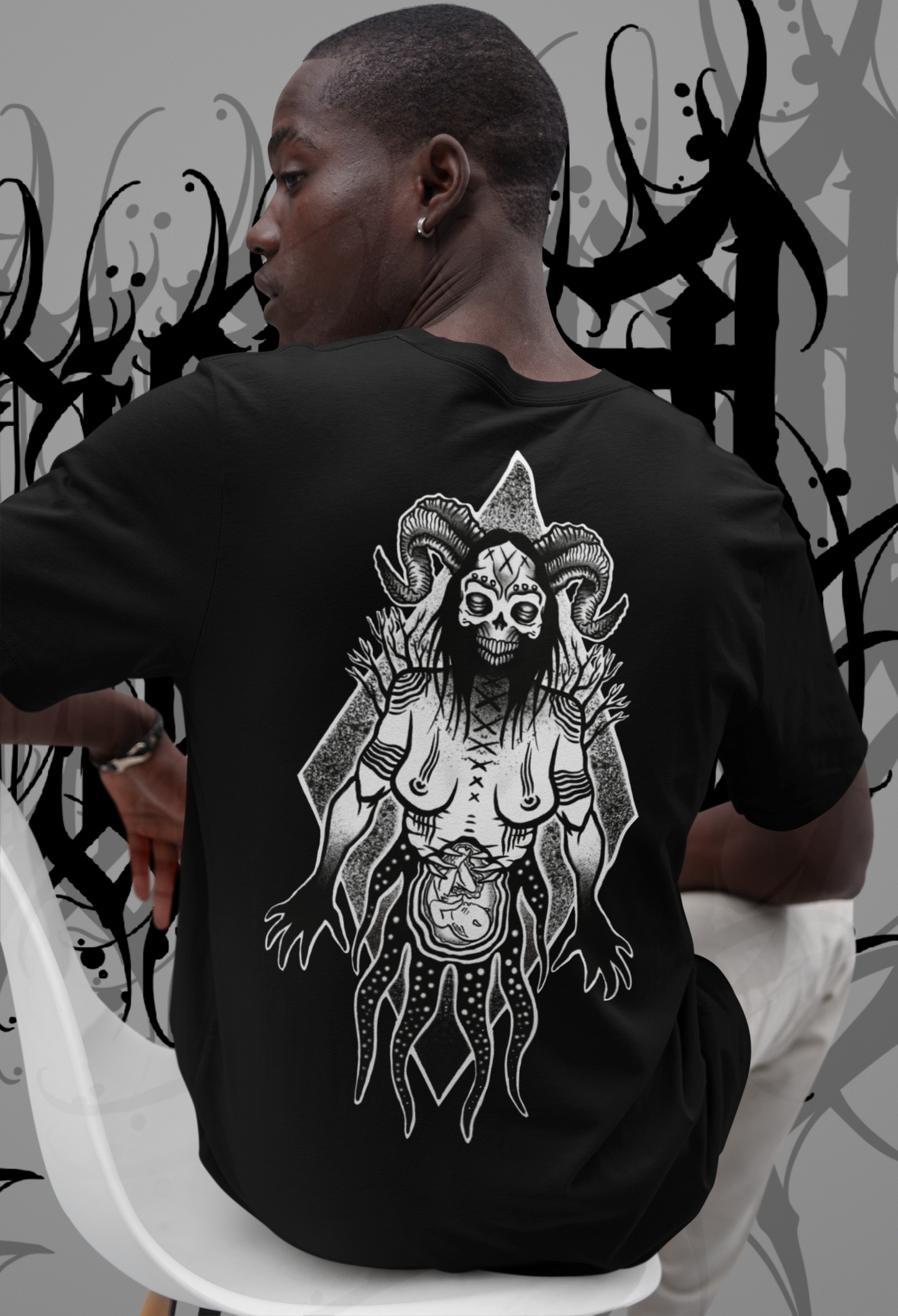 male model sitting on a chair showing back view of hex culture tshirt by venom culture. featuring gothic witchy design by Rachel bones tattoo