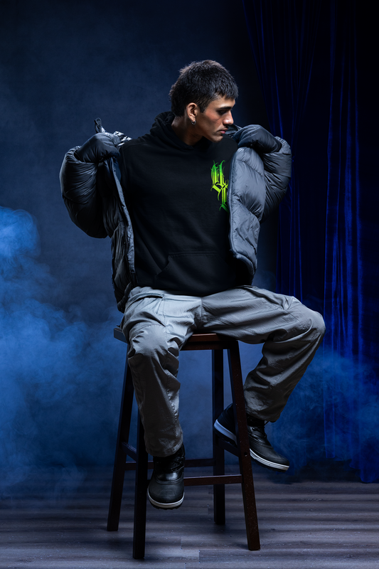 man sitting on stool taking off puffer jacket to reveal black hoodie with green gothic calligraphy venom culture logo